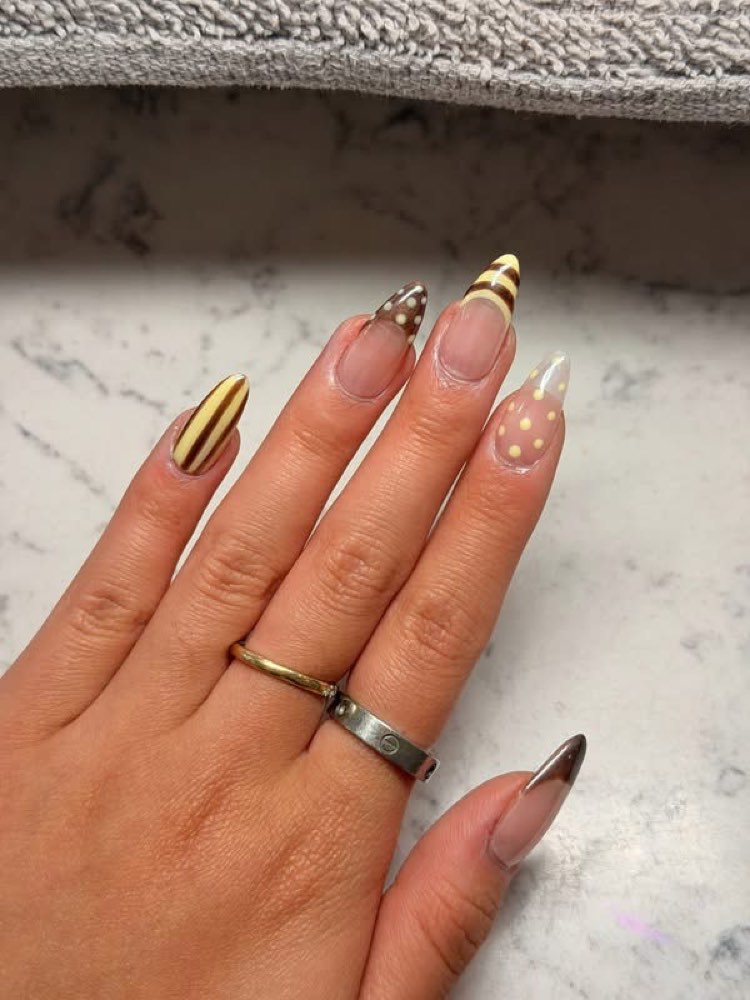 Almond nails with chocolate and yellow polka-dot French tips on marble