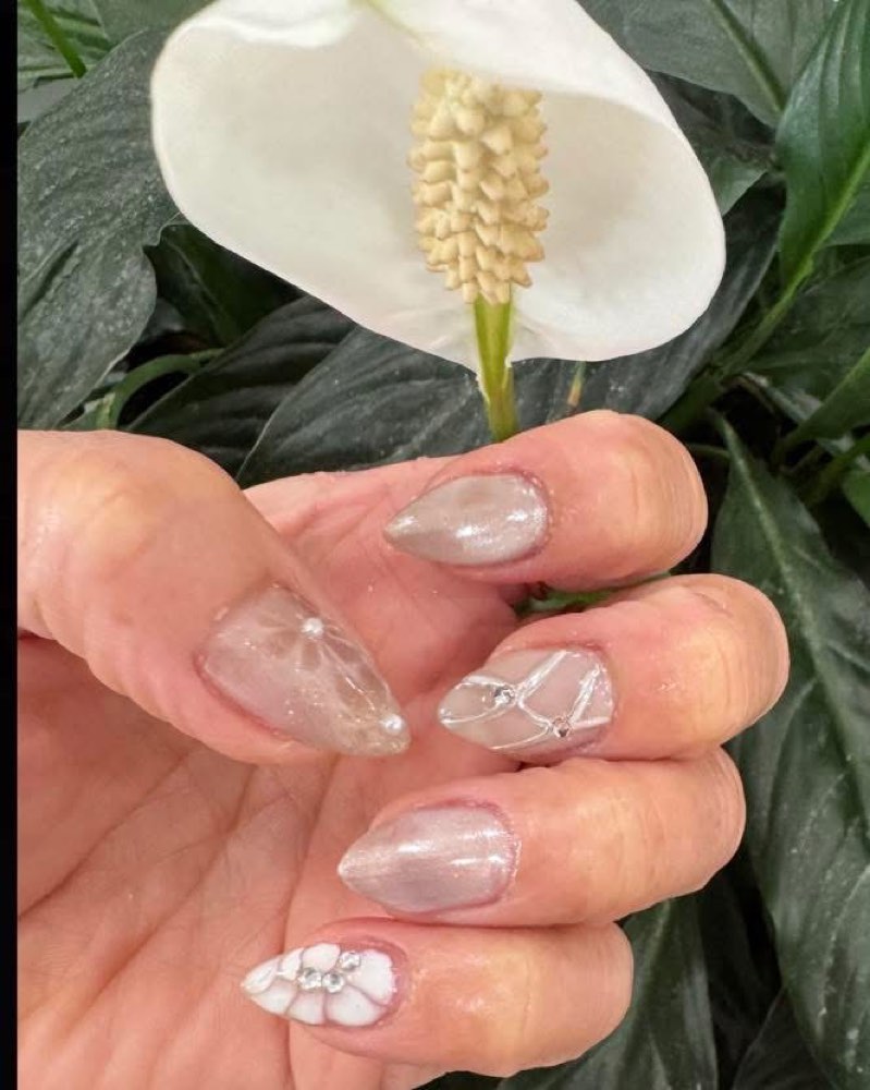 Milky aura nails with pearl and crystal details against greenery