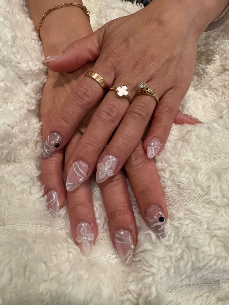 Sheer pink oval nails with white swirl art and small black gems